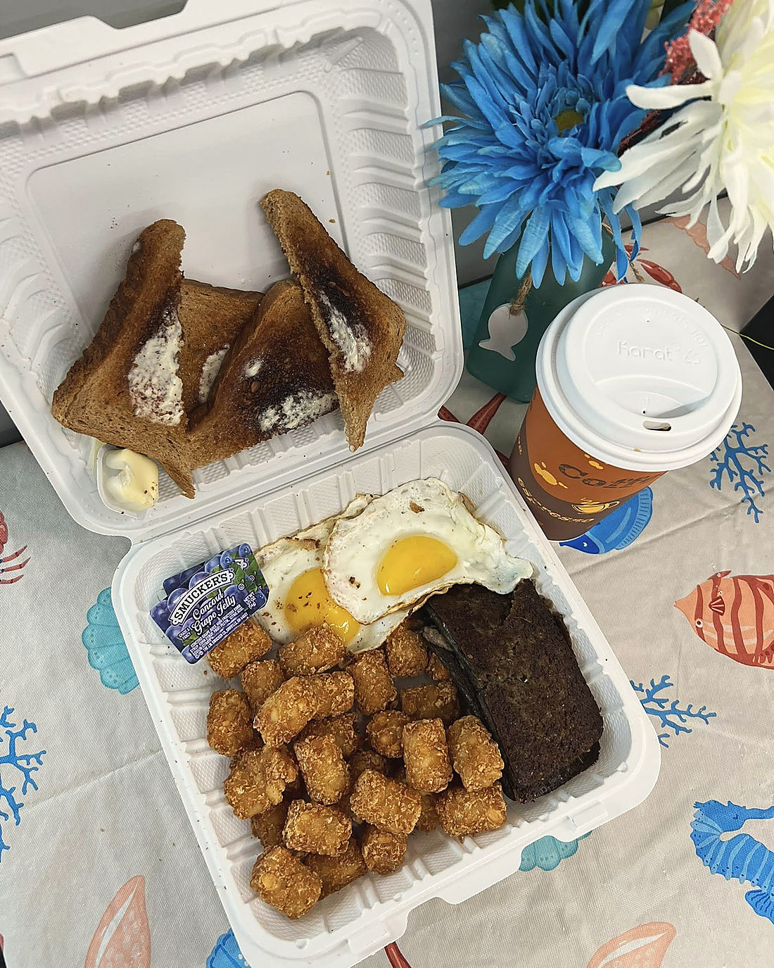 A carry-out breakfast: two eggs, scrapple, tater tots, buttered toast and a coffee