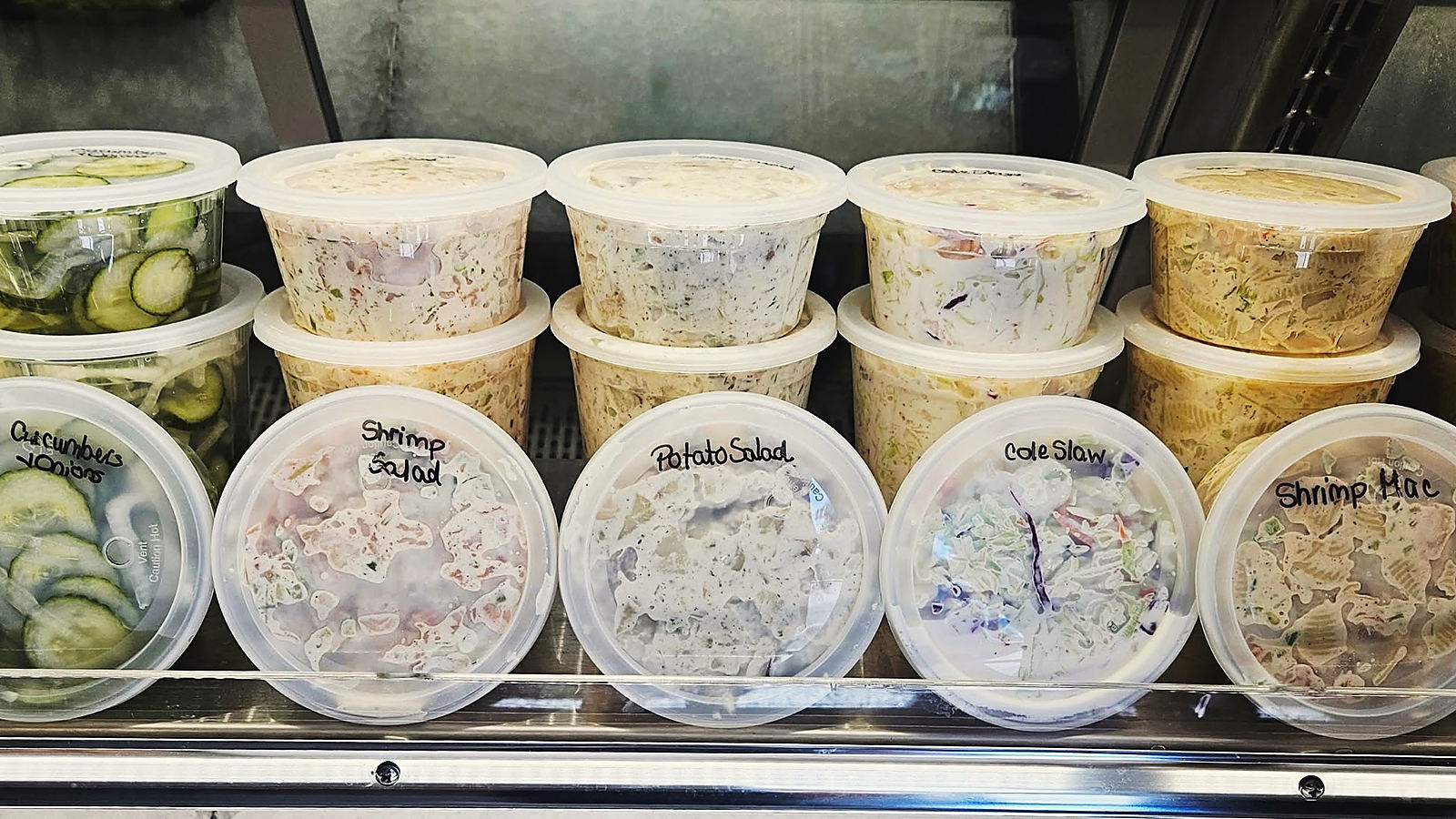 Deli tubs in the cold case, hand-marked Cucumber, Shrimp Salad, Potato Salad, Cole Slaw and Shrimp Mac